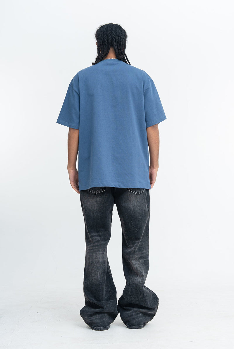 Back view of an oversized blue streetwear graphic tee worn with loose black jeans on a model against a white background