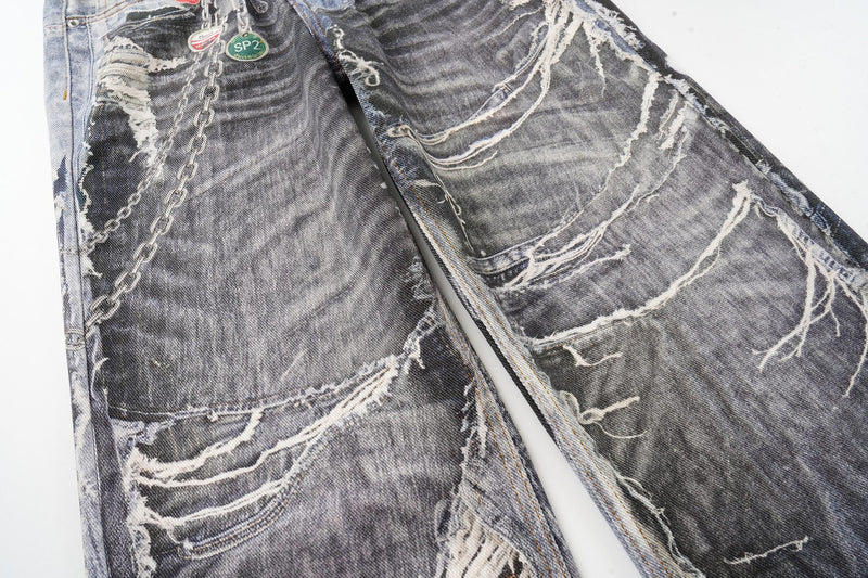 Front upper-leg view of distressed patchwork jeans with chain graphic and ripped details