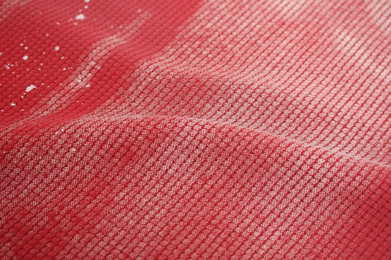 Close-up of red washed cotton fabric with textured weave and faded streetwear-style distressed finish
