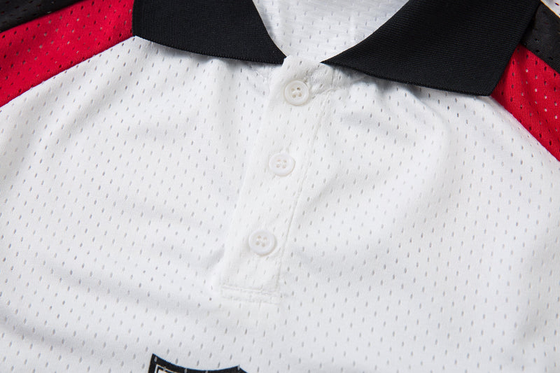 Close-up of a white mesh polo shirt with black collar and red colorblock shoulder panels, featuring a button placket