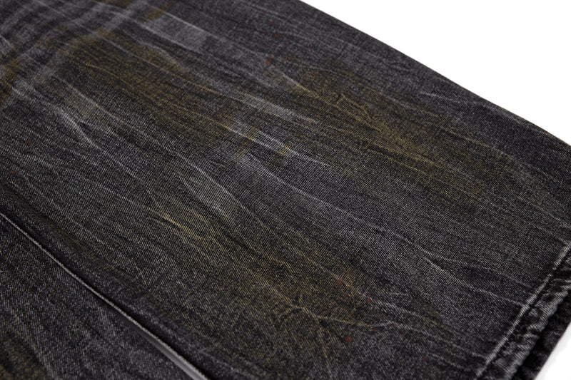 Close-up of black denim leg with subtle faded stains and grain texture