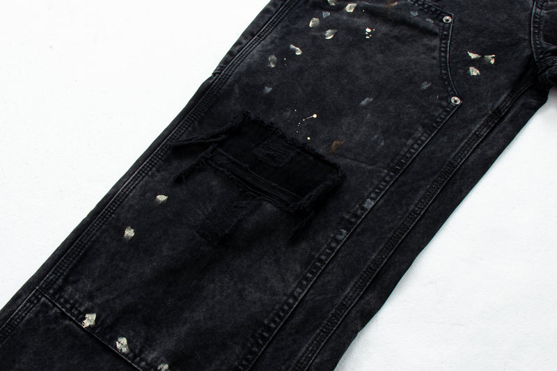 Close-up of black denim leg with large frayed knee rip and paint splatter