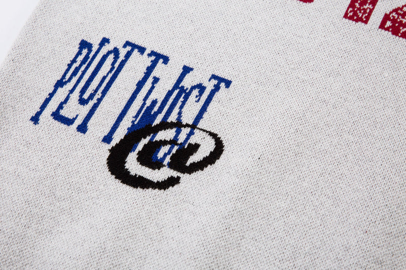 Close-up of blue embroidered text and black crest graphic on white knit sweater