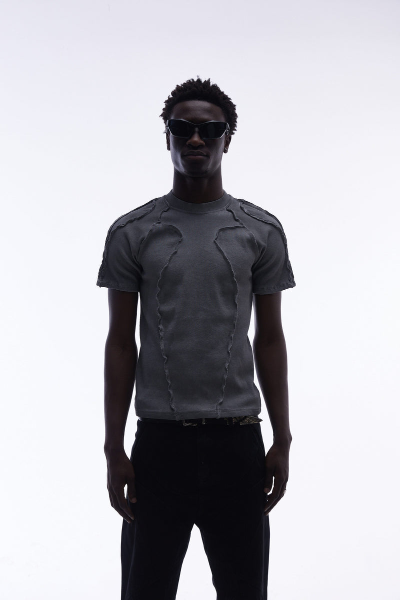 Dark gray deconstructed compression tee with raw seam detailing, styled on a model with black sunglasses