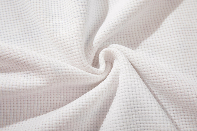 Close-up of soft white waffle-knit fabric with subtle texture and folded drape for a vintage ringer T-shirt