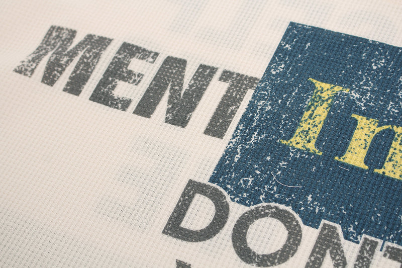 Close-up of distressed black text and blue graphic block on cream waffle fabric