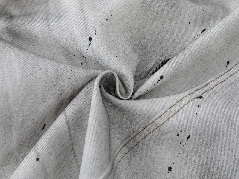 Close-up of white denim shorts fabric with black paint splatter and curved seam stitching