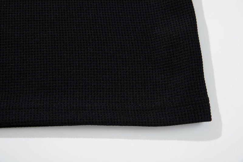Black textured cotton tee fabric with a subtle woven pattern and clean hem detail on a white background