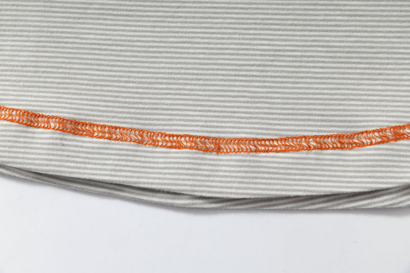 Close-up of a light gray striped T-shirt hem with bright orange contrast stitching on soft ribbed fabric