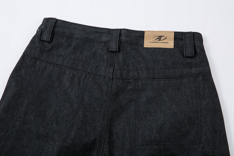 Back waistband close-up of dark denim pants with tan logo patch and belt loops