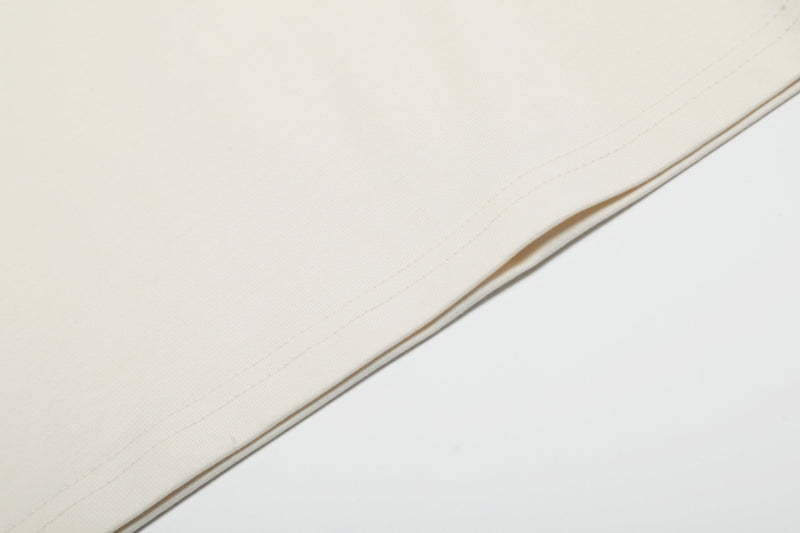 Close-up of a cream graphic T-shirt hem with subtle stitching and soft cotton fabric texture