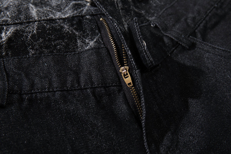 Close-up of gold zipper detail on black denim pants with cracked panel fabric