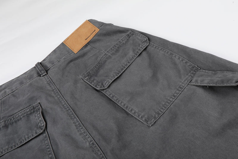Close-up of gray cargo shorts back pocket flap and tan logo patch at the waistband