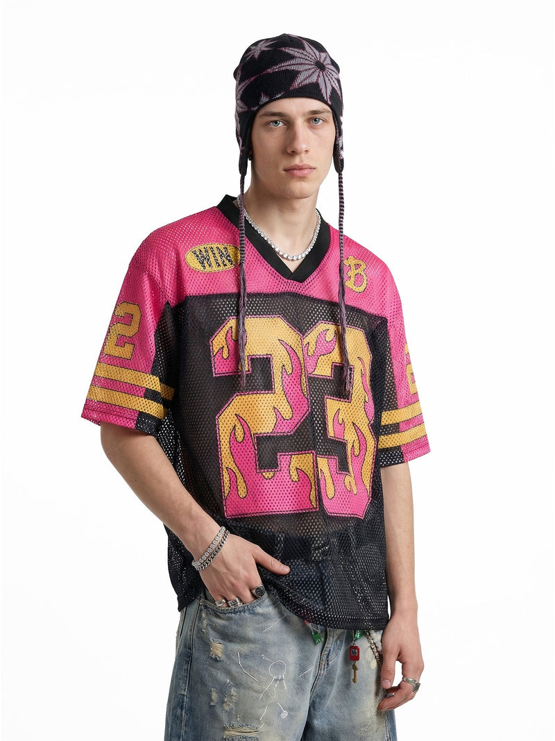 Model wearing a pink and black mesh jersey T-shirt with flame number 23, paired with distressed jeans and a knit hat