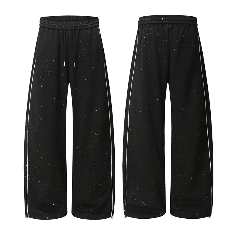 Black wide-leg track pants with speckled galaxy print, white side piping, and zippered hems, shown front and back