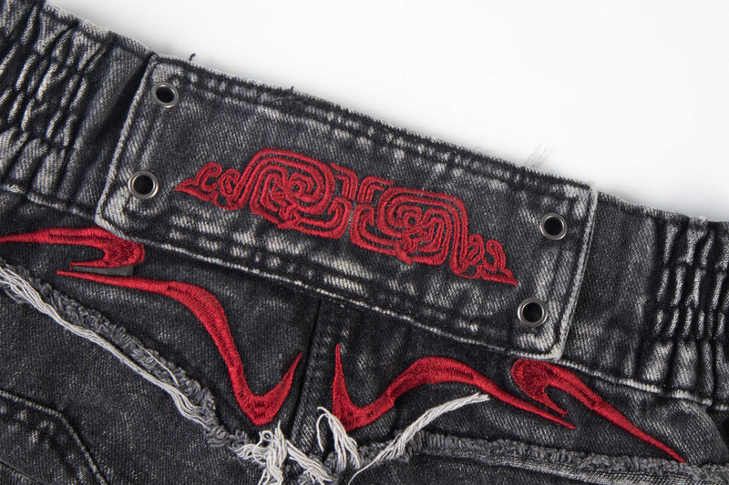 Close-up of embroidered red graphic on the back waistband of faded black denim