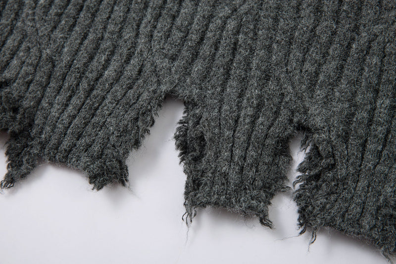 Close-up of frayed charcoal gray sweater hem with torn openings