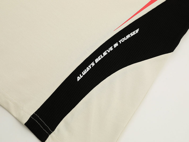 Close-up of a beige athletic tee with black curved side panel, red accent stripe, and bold white lettering