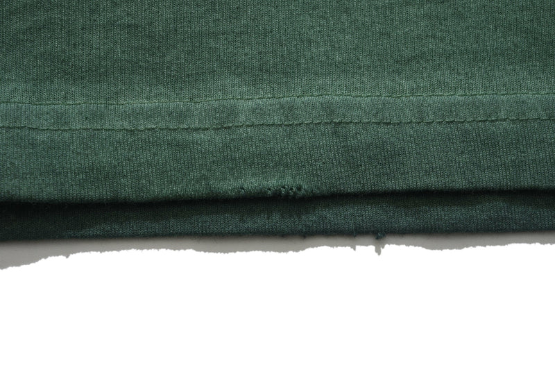 Close-up of a vintage wash green graphic tee hem with raw edge and soft faded cotton texture