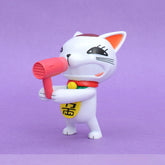 The Dandadan Lucky Cat PVC Figure stands 9.5 cm tall, showcasing a kawaii white cat with a red collar and bell joyfully holding a pink hairdryer. It features large black eyes and a yellow symbol on its belly, popping against its purple background—a perfect addition to any anime figure collection.