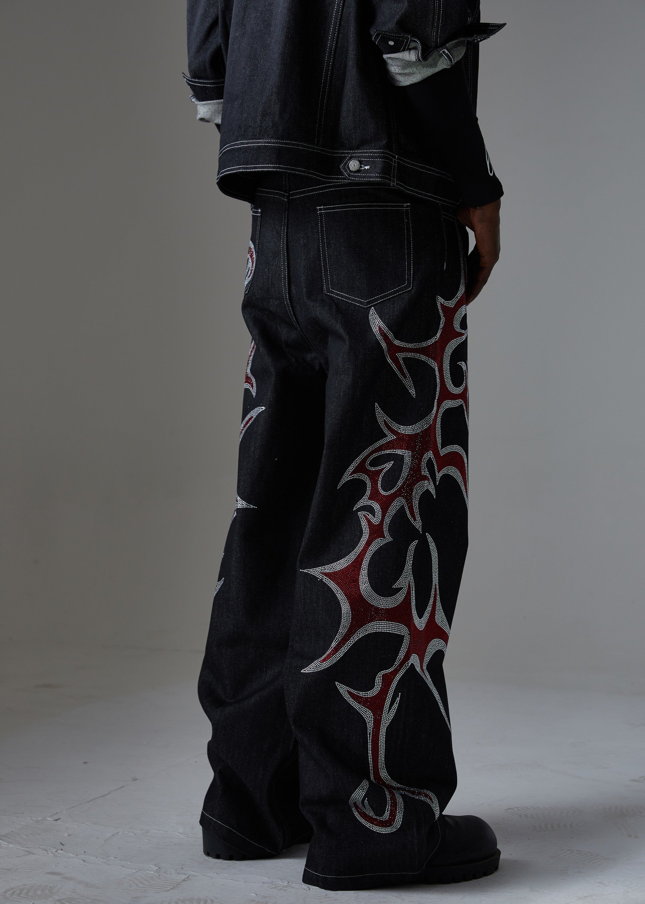 Side view of black wide-leg denim pants with red and silver rhinestone tribal flame graphic on the leg
