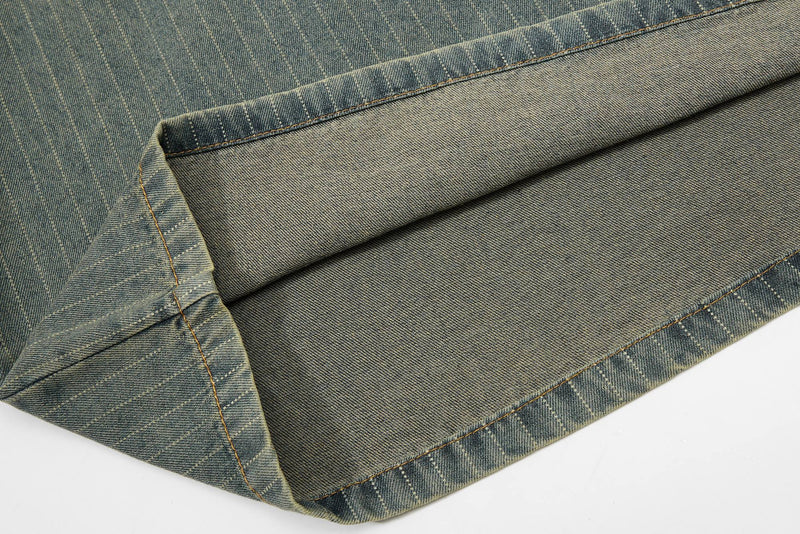 Close-up of vintage pinstripe denim fabric with folded hem and visible contrast stitching, showing a rugged streetwear texture