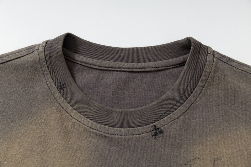 Close-up of a washed vintage streetwear tee with ribbed crew neck and subtle abstract sketch details on olive brown fabric