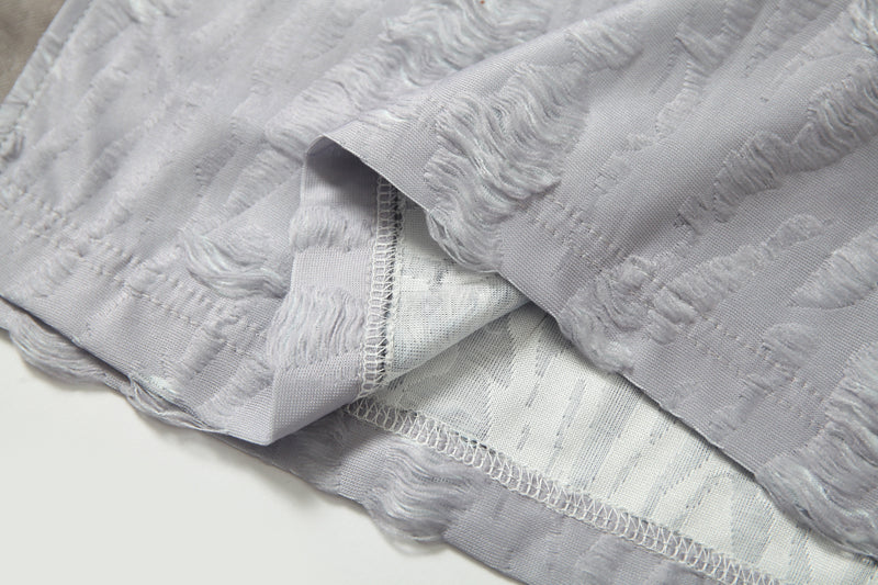Close-up of light gray textured mesh tee with distressed patchwork panels and visible overlock seams