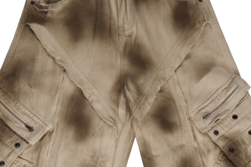 Close-up of front thigh panels on distressed cargo barrel pants with diagonal seam details and zip pockets