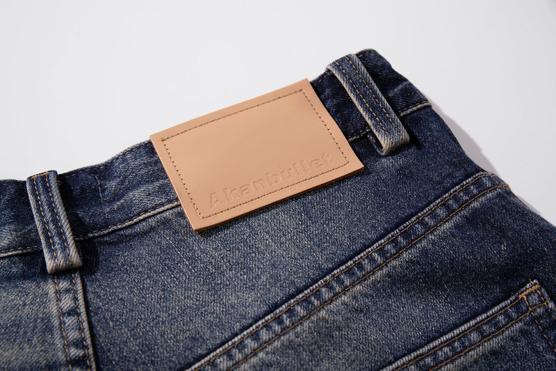 Close-up of tan leather waistband patch and belt loops on mid-blue washed denim