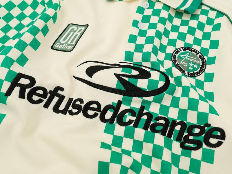 Close-up of cream jersey front showing green checkered print, patches, and black logo text