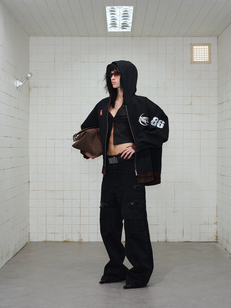 Model in black zip hoodie with hood up, holding a brown bag, front graphics visible
