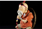 The Seakoff Master Roshi Collectible Figure displays the iconic Dragon Ball character at 18cm, featuring his white beard, bald head, sunglasses, orange clothing, and a large backpack. He is accompanied by his trusty stick and banana fan against a black backdrop in this premium action statue.