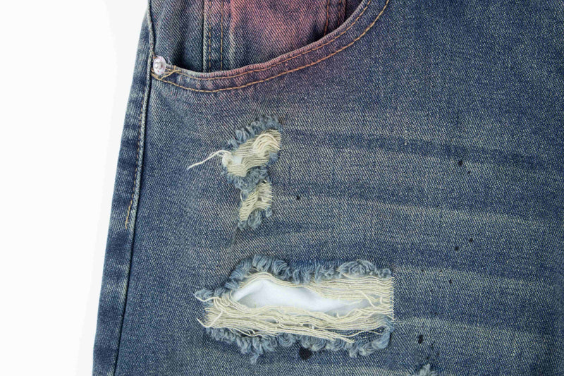 Close-up of a ripped front pocket on blue distressed jeans with worn frayed edges