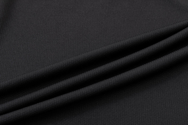 Close-up of black textured fabric with folded drape, showing the material for a vintage plaid panel polo shirt