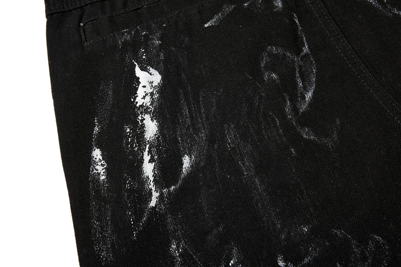 Close-up of black denim leg with white paint-like wash marks and stitched pocket seam