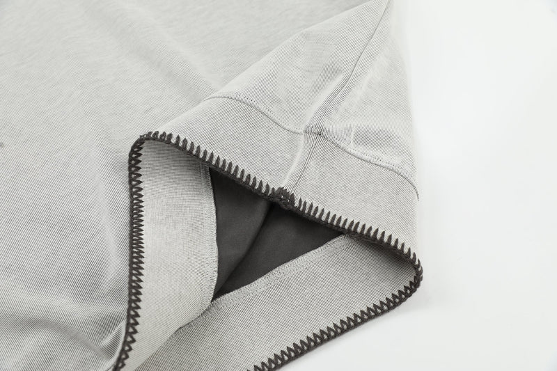 Close-up of a light gray Henley tee sleeve with contrast black stitching and relaxed ribbed cotton fabric
