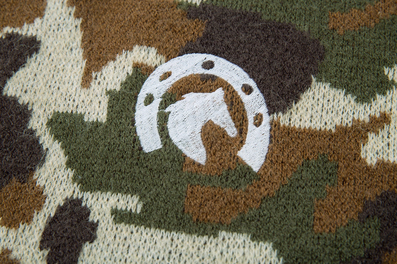 Close-up of embroidered logo patch on olive, brown, and cream camouflage knit