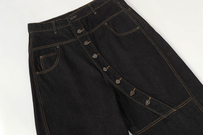 Three-quarter front view of black asymmetric button denim pants with wide balloon legs