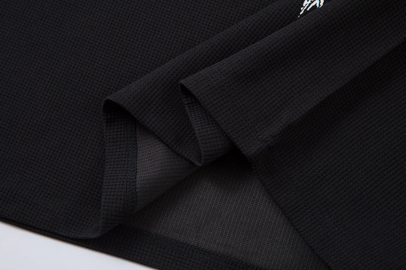 Black textured polo shirt fabric with a subtle gothic cross graphic, shown in a close-up fold detail