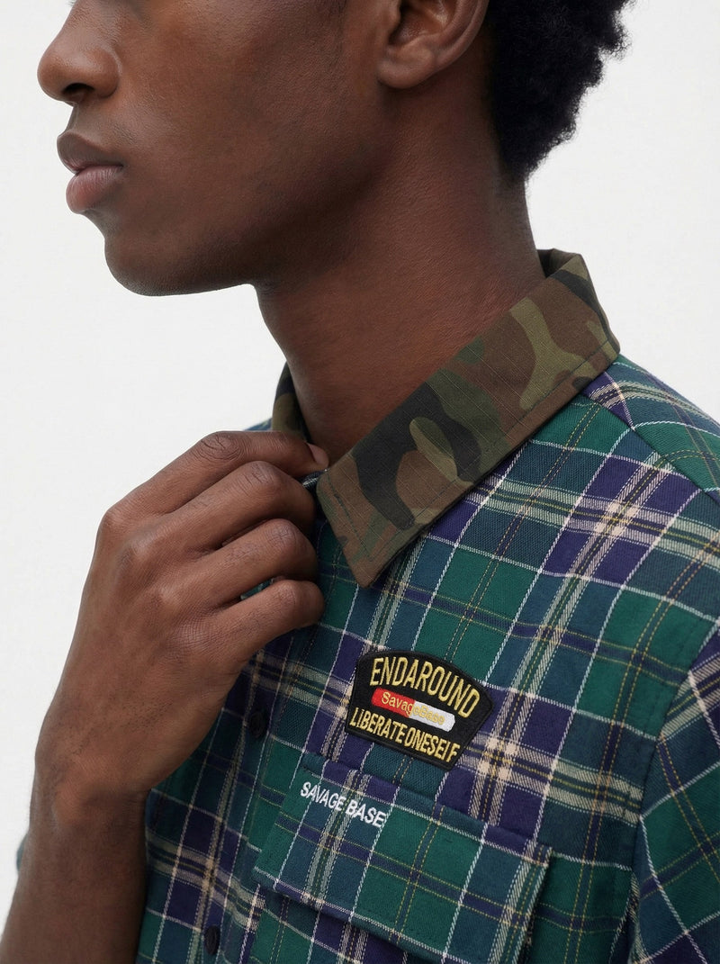 Close-up of a green plaid shirt with camouflage collar, streetwear patch detail, and a hand adjusting the neckline