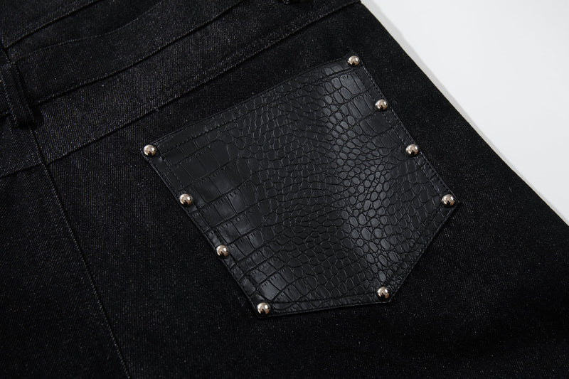 Close-up of black faux crocodile back pocket on denim pants with metal rivets