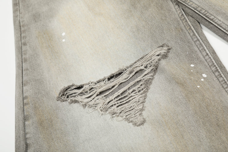 Close-up of ripped knee on faded gray jeans with frayed edges and paint splatter