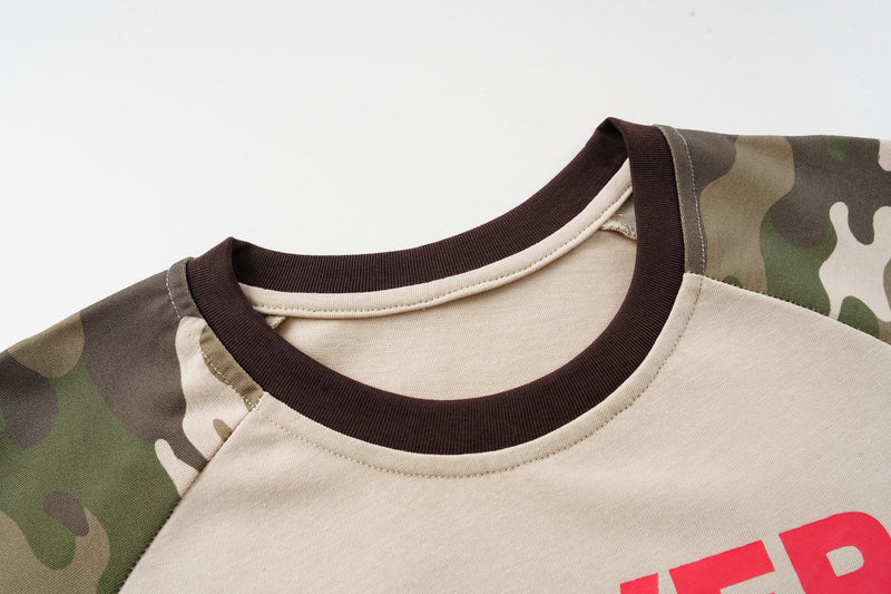 Close-up of a camo raglan T-shirt with brown ribbed crew neck and bold red streetwear graphic on beige fabric
