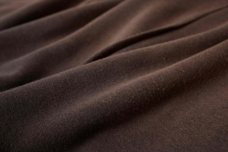 Close-up of dark brown cotton tee fabric with sculpted folds and raw seam texture, showcasing an avant-garde streetwear look