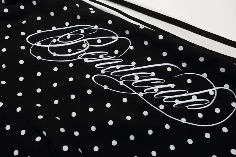 Close-up of black polka dot shorts showing white script graphic and side stripes