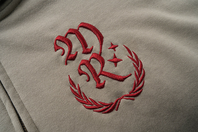Close-up of red embroidered monogram and wreath graphic on taupe hoodie