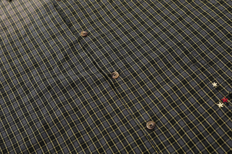 Close-up of a black and yellow gradient plaid shirt with distressed texture, buttons, and raw-edge detail