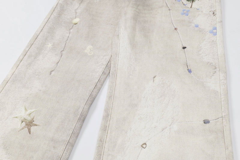 Close-up of upper leg on washed botanical print jeans with blue flower and palm tree details