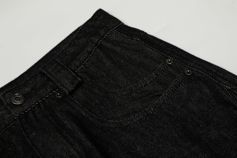 Close-up of black denim waistband and front pocket area showing button, loops, and seam detail